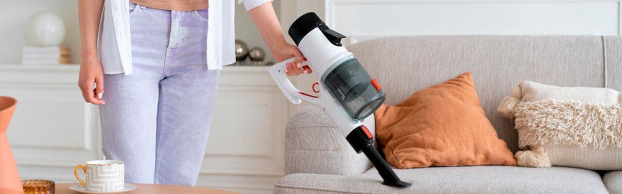 Mujer aspirando sillón con una limpiadora portatil